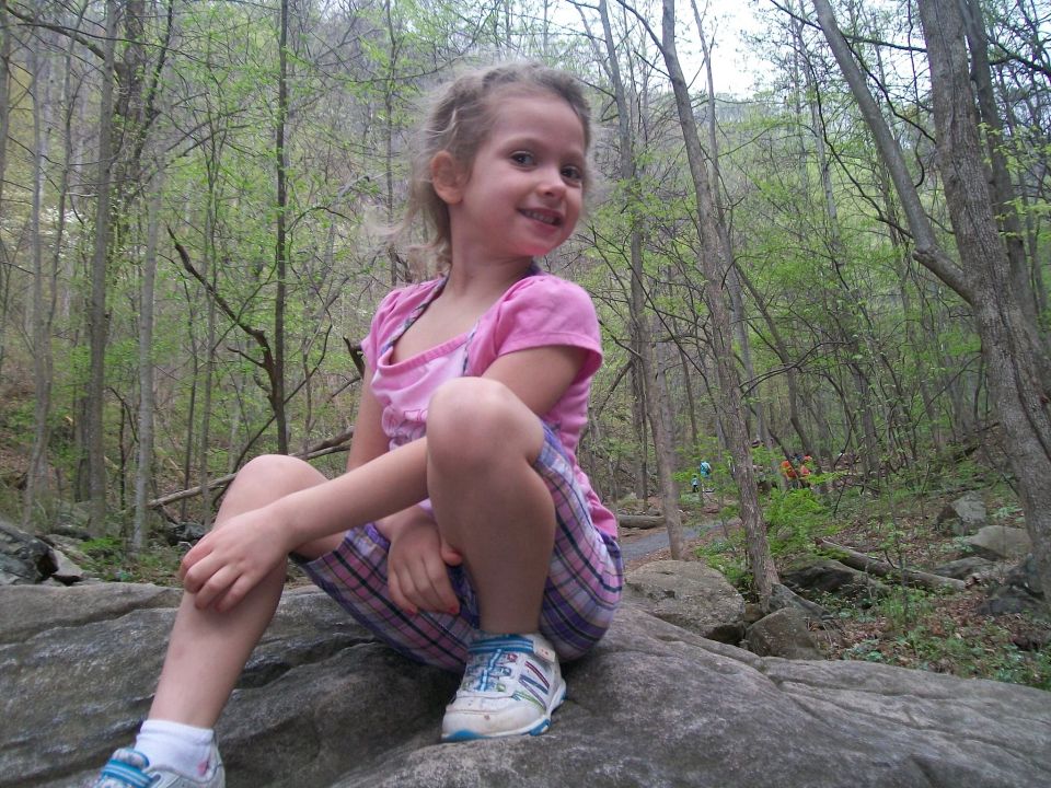 Photo of a child sitting on rocks in a wooded area