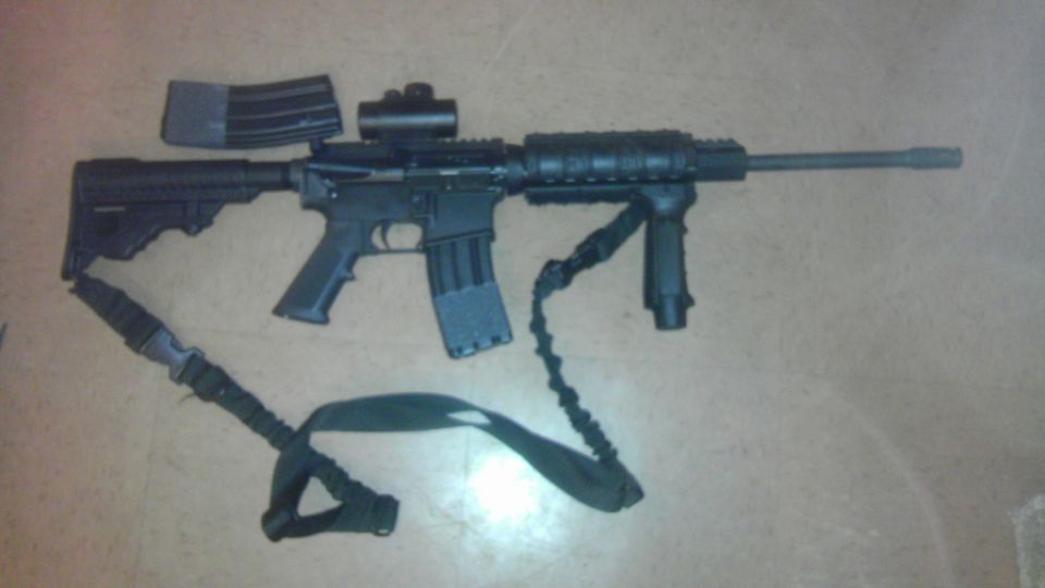 AR-15 style rifle with two magazines, red dot sight, vertical foregrip, and sling