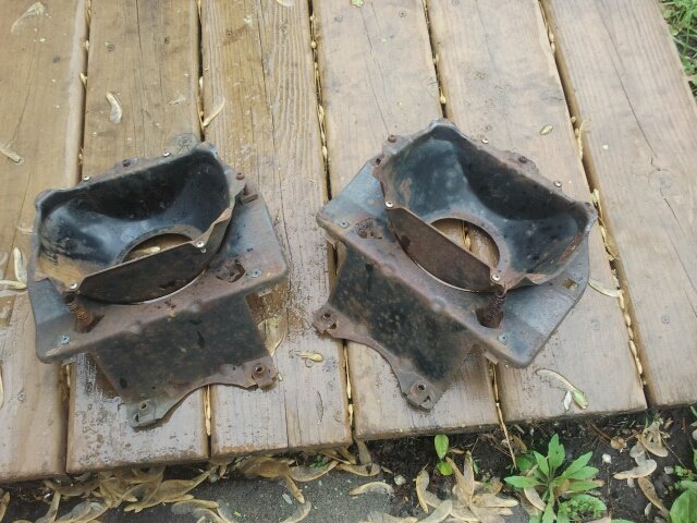 Two rusty, black metal parts with circular openings, resting on wooden planks