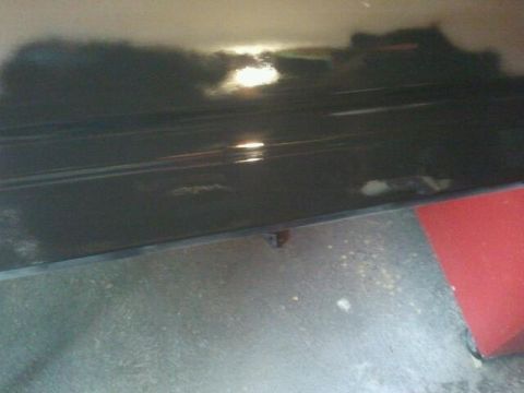1979 Ford Bronco - A close-up view of a dark-colored vehicle panel shows reflections of light and the surrounding environment.