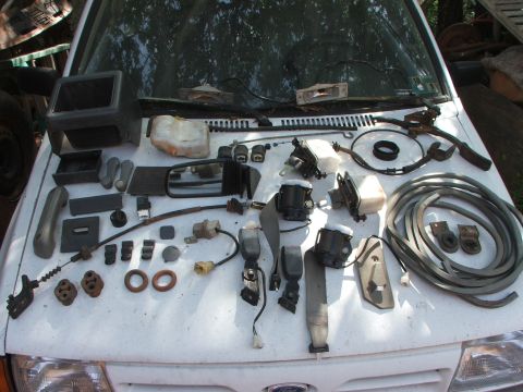 1991 Ford Festiva - Various car parts are arranged on the hood of a white vehicle, possibly for sale or repair.