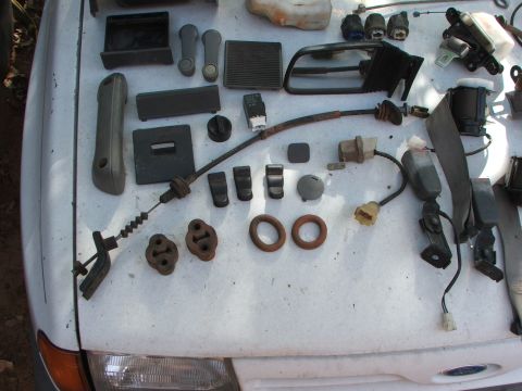 1991 Ford Festiva - Various car parts are spread out on the hood of a white vehicle.