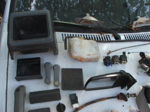 1991 Ford Festiva - Various interior and exterior car parts are displayed on a vehicle's dashboard, suggesting a restoration or parts inventory.