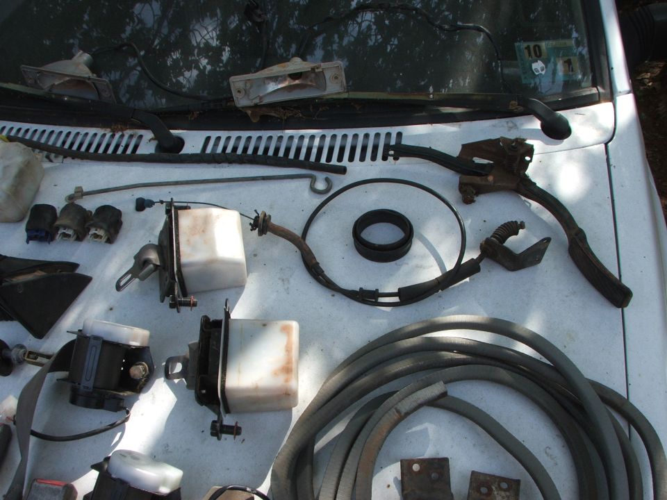 Various car parts including brake fluid reservoirs, seat belts, and hoses laid out on a white car hood