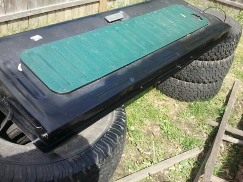 1979 Ford Bronco - A black tailgate, possibly from a Ford Bronco, is shown outdoors, propped up on tires.