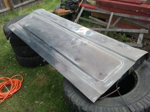 1979 Ford Bronco - A bare metal tailgate is shown resting on a stack of tires, with various outdoor debris visible.