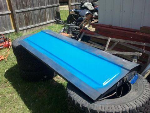 1979 Ford Bronco - A blue tailgate is shown resting on a stack of tires outdoors.