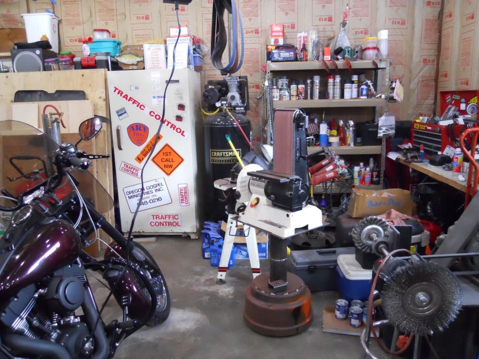 Motorcycle parked in a workshop with a sander, air compressor, and shelves of supplies