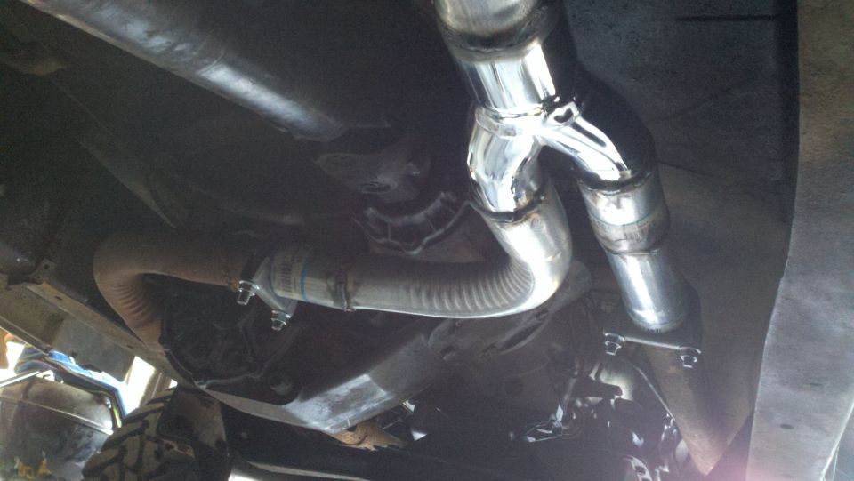 Underside view of a vehicle's exhaust system with a Y-pipe and flexible tubing