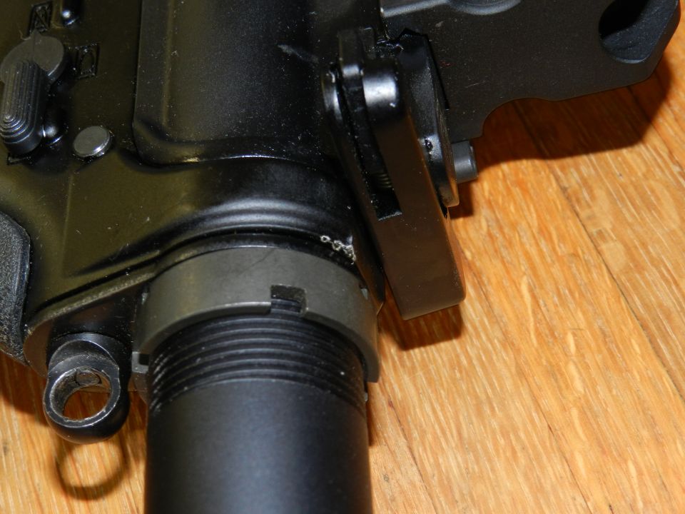 Black firearm receiver with a silver pin and a black lever. The part is on a wooden surface