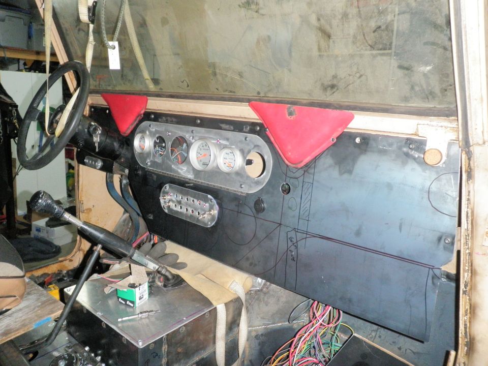 Interior view of a vehicle dashboard with aftermarket gauges, a steering wheel, and exposed wiring. The dashboard panel has layout lines drawn on it