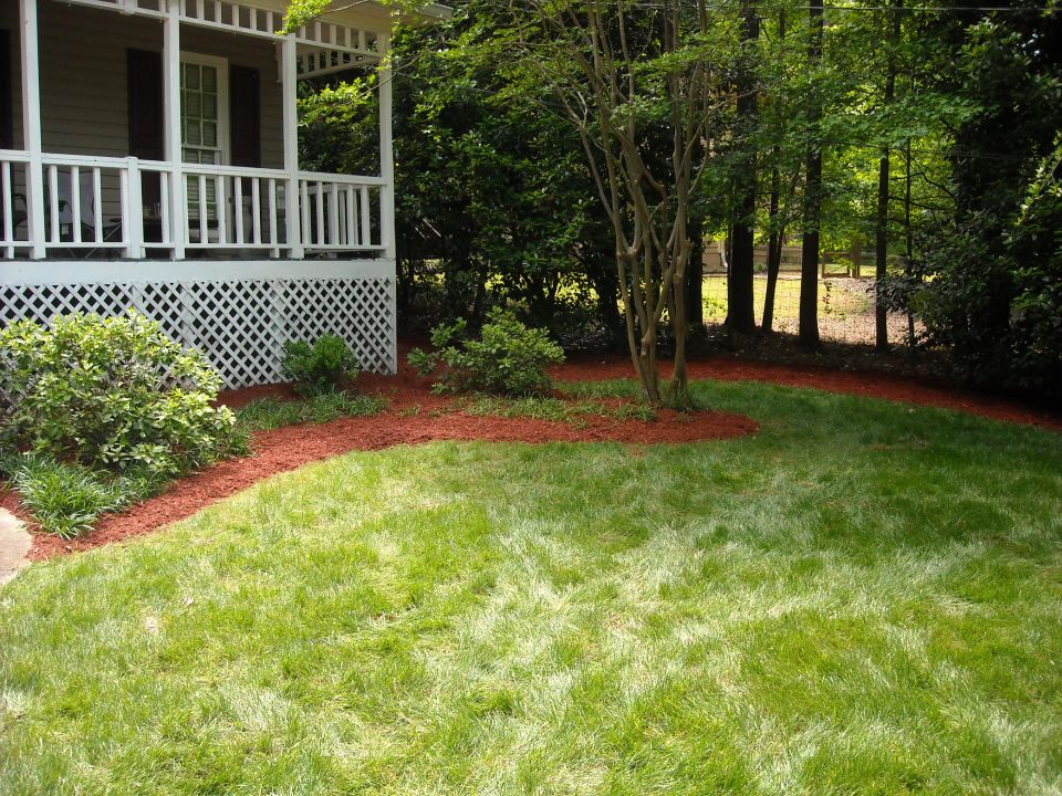 Front yard with a white porch, green grass, and trees