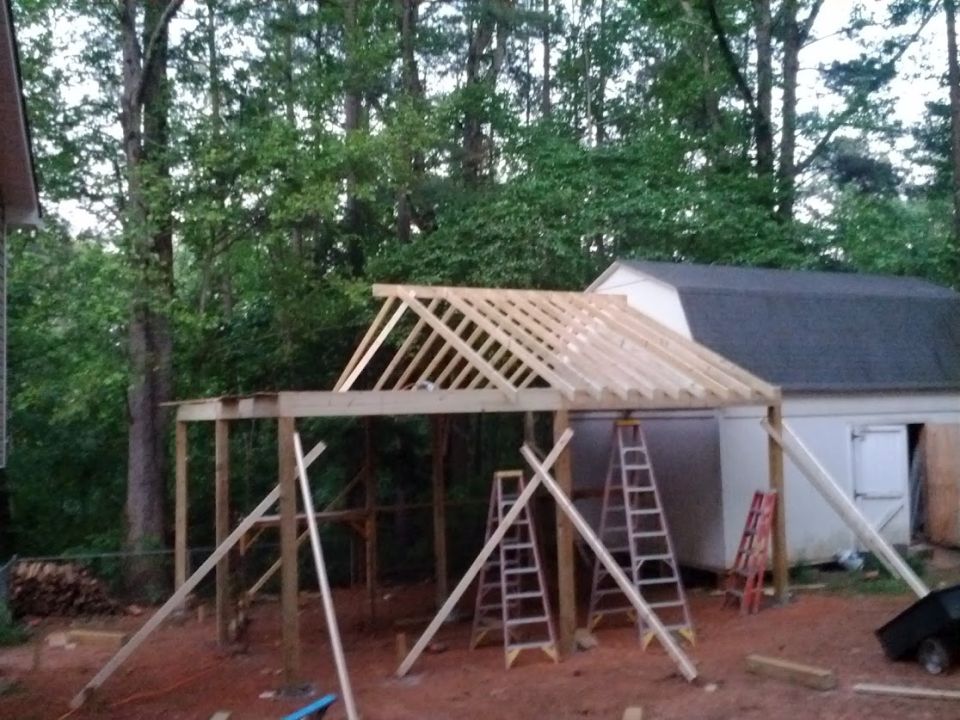 Construction site with unfinished roof framing and a white shed