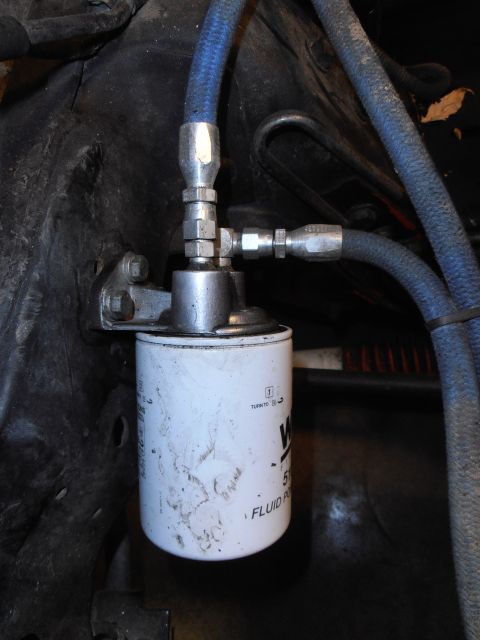 1990 Ford Bronco - Close-up view of a white fluid filter with blue hoses attached to a metal fitting.