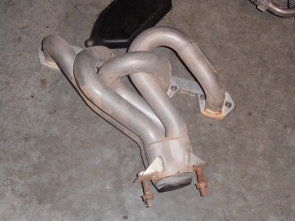 Exhaust manifold with four pipes merging into one, resting on a concrete floor