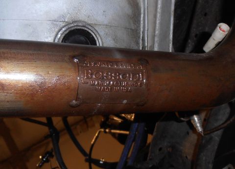 1990 Ford Bronco - Close-up of an exhaust pipe with a Bossoni Manufacturing plate, indicating it was made in the USA.