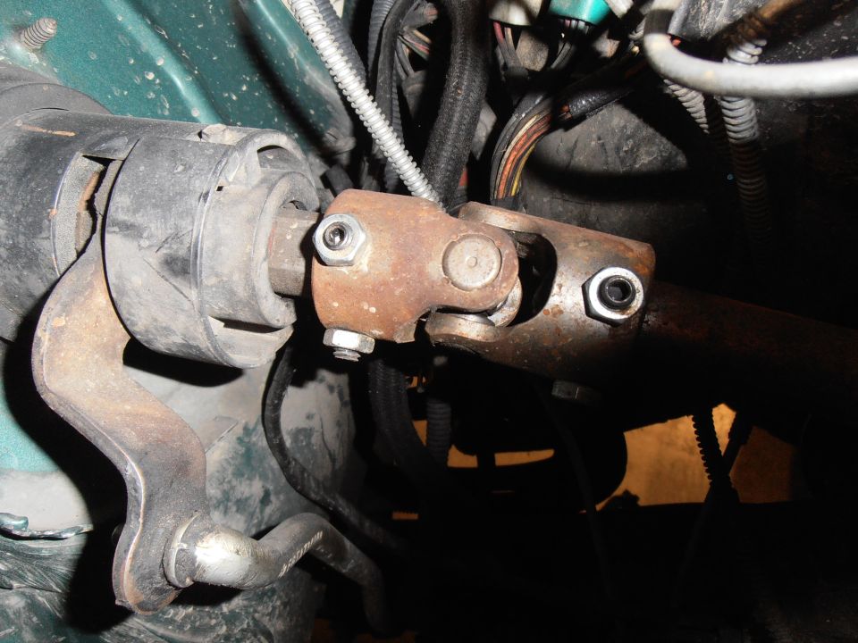 Close-up of a rusty steering shaft universal joint with bolts and wiring harness