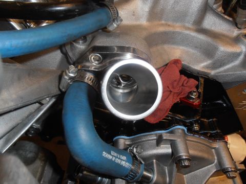 1990 Ford Bronco - Engine-bay close-up of a polished stainless thermostat housing bolted to the intake manifold, with the thermostat visible inside the open n…