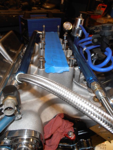1990 Ford Bronco - A close-up view of an engine's fuel rail system, blue fuel lines and a pressure gauge, with a section covered in blue tape.