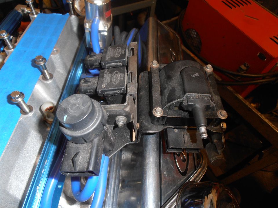 Black emissions solenoids and ignition coil on bracket over blue engine part