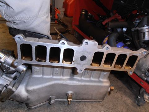 1990 Ford Bronco - An engine intake manifold is shown, with visible ports and attached plumbing components.
