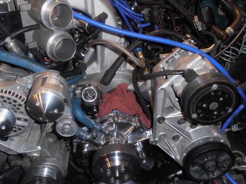 1990 Ford Bronco - Detailed view of various engine components, including a supercharger and AC compressor, with blue hoses and a red rag.