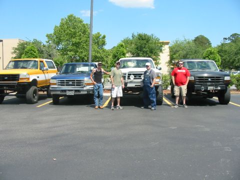 1992 Ford Bronco - Four men stand in front of their lifted trucks in a parking lot on a sunny day.