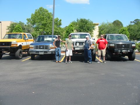 1992 Ford Bronco - Four trucks, including a yellow and white 1992 Ford Bronco, are parked in a lot with four men standing in front of them.