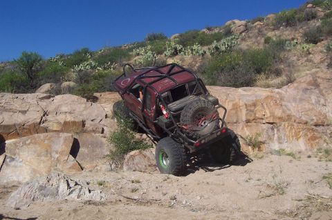 1981 Ford F-150 - A heavily modified pickup truck navigates a steep, rocky incline under a clear blue sky.
