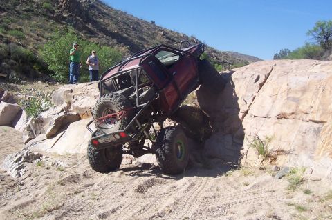 1981 Ford F-150 - A heavily modified pickup truck is wedged between rocks on a sandy, off-road trail.
