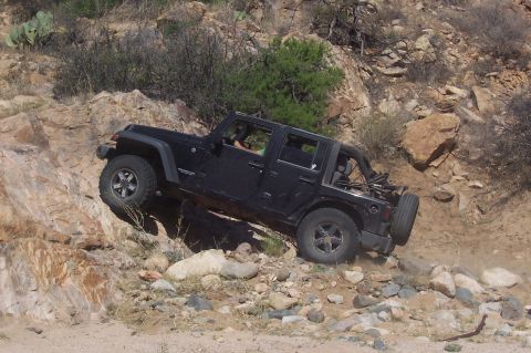 1981 Ford F-150 - Jeep Wrangler tackling off-road obstacles on a dusty, rocky incline.