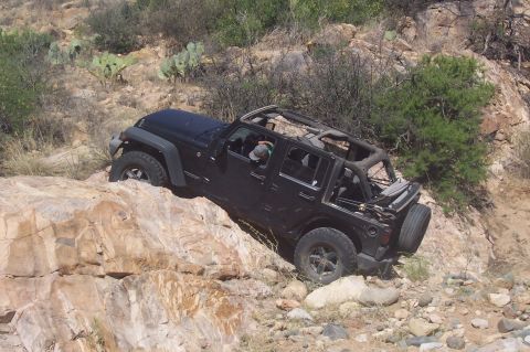 1981 Ford F-150 - A black Jeep Wrangler navigates a rocky, off-road trail with its top removed.