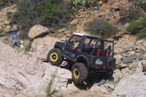 1981 Ford F-150 - A modified Suzuki Samurai navigates a challenging rocky trail with a person observing.