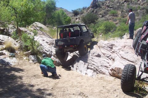 1981 Ford F-150 - Multiple off-road vehicles are navigating a challenging rocky trail under a clear sky.