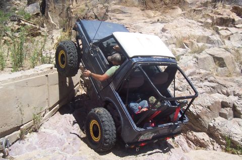 1981 Ford F-150 - An off-road vehicle navigates a steep, rocky incline, with one wheel significantly elevated.