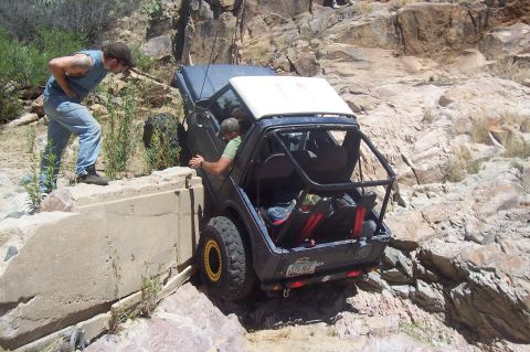 1981 Ford F-150 - Two people assist an off-road vehicle as it navigates a steep, rocky incline next to a concrete structure.