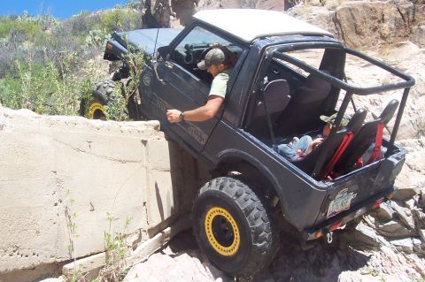 1981 Ford F-150 - A Suzuki Samurai is shown off-roading on a rocky, uneven surface with a driver and passenger inside.