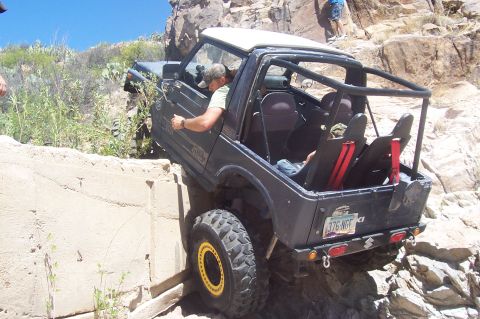 1981 Ford F-150 - An off-road vehicle attempts to climb a steep, rocky terrain with a concrete barrier on the left.