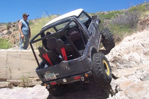 1981 Ford F-150 - A modified off-road vehicle navigates a steep, rocky incline under a clear blue sky.
