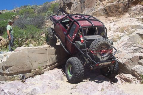1981 Ford F-150 - A heavily modified red truck navigates a rocky incline, its off-road capabilities.