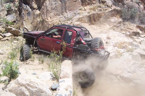 1981 Ford F-150 - A modified red truck tackles a challenging off-road course, kicking up dust on the rocky terrain.