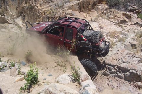 1981 Ford F-150 - This heavily modified truck navigates a challenging rocky incline, kicking up dust as it climbs.