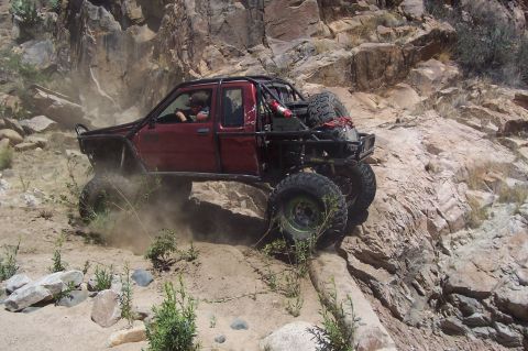 1981 Ford F-150 - Off-road pickup truck navigates challenging rocky terrain with dust kicking up.