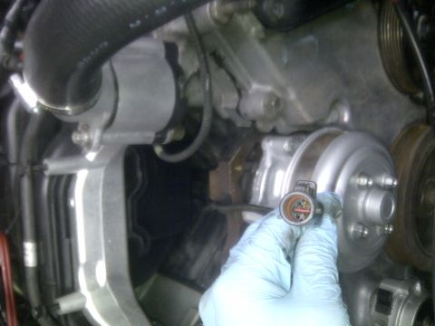 2000 Ford Crown Victoria - A hand holds an electrical connector near an engine component, with the Supermotors logo visible at the bottom.