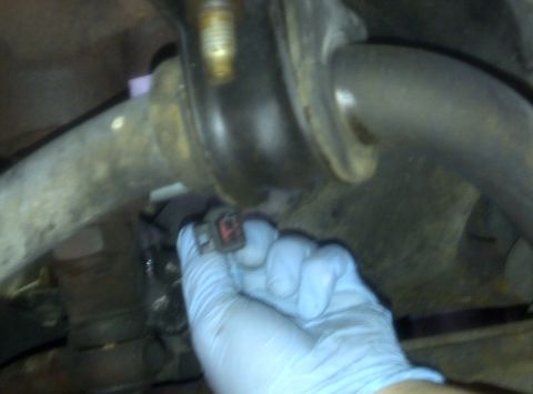 2000 Ford Crown Victoria - A gloved hand holds an electrical connector near a vehicle's suspension system.
