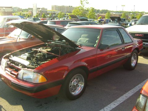 2007 Ford Mustang - Red coupe parked at an outdoor event, hood raised to reveal the engine.