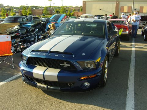 2007 Ford Mustang - A blue 2007 Ford Mustang Shelby GT500 with white racing stripes is parked in a lot with other vehicles.