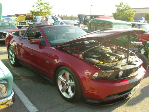 2007 Ford Mustang - A red convertible sports car is parked at an outdoor event with its hood open, revealing the engine compartment.