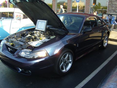 2007 Ford Mustang - A dark purple Ford Mustang is displayed with its hood open, revealing the engine and a framed certificate.