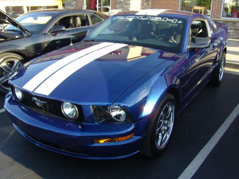 2007 Ford Mustang - A blue 2007 Ford Mustang with white racing stripes and a ROUSH banner is parked next to another vehicle.